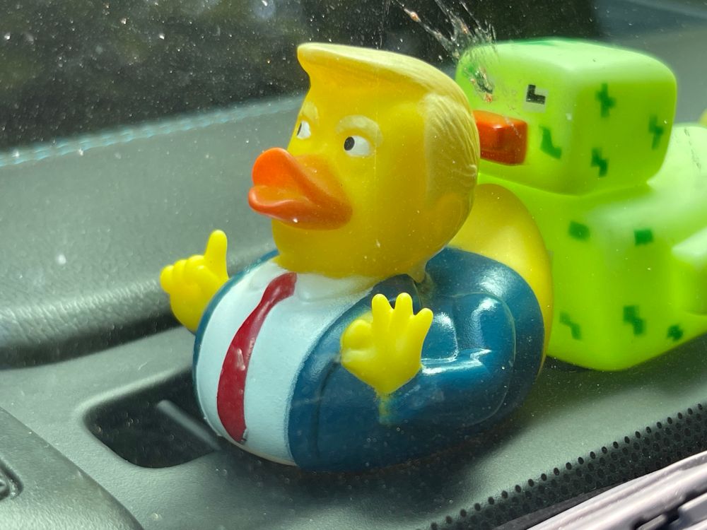 DJT rubber duckie on dashboard wearing red tie & blue jacket.