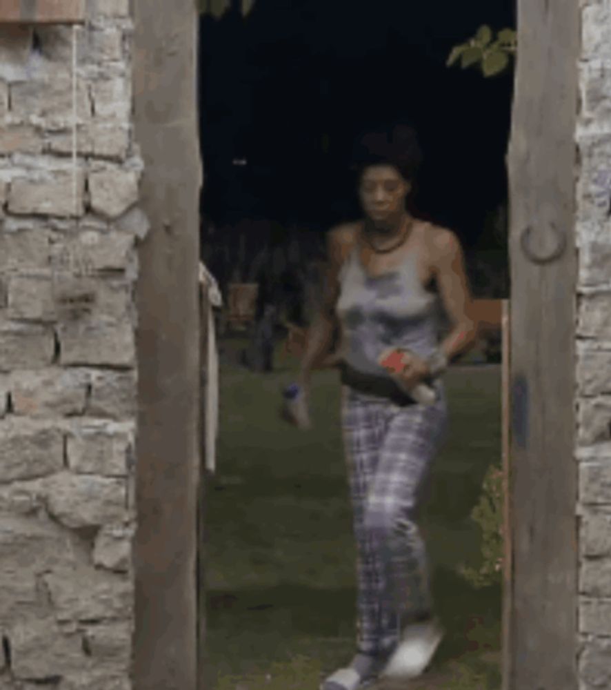 a woman in a tank top and plaid pants is walking through a stone door