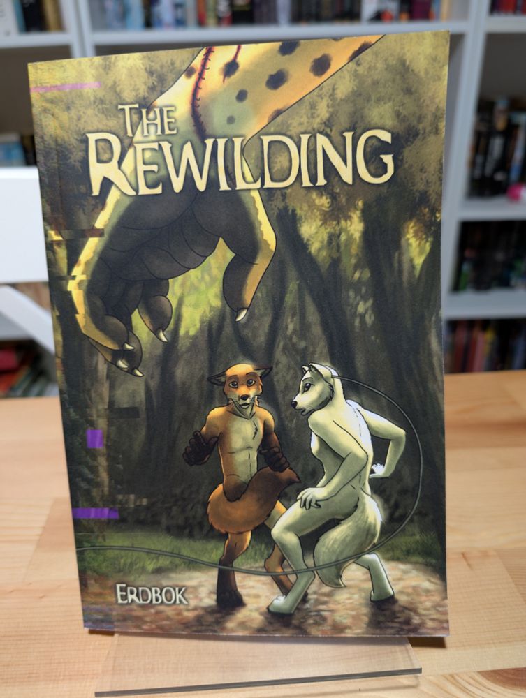Photo of a print book, The Rewilding by Erdbok, which features two anthropomorphic characters cowering. The bleeding hand of a third anthropomorphic character is in the foreground.
