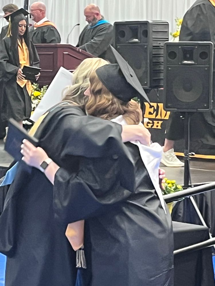 A girl at her high school graduation hugging one of her faculty members