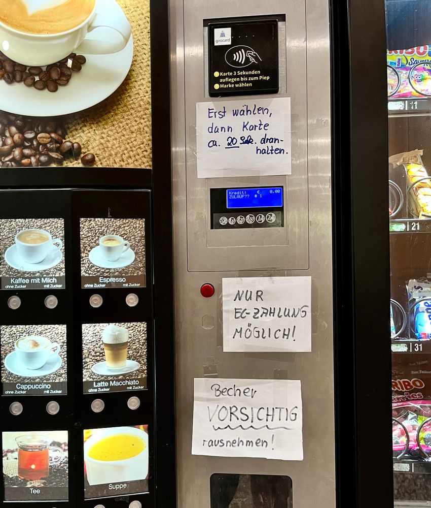Kaffeeautomat im Krankenhaus mit drei handgeschriebenen Zetteln die Hinweise zur Benutzung geben, weil die offenbar ziemlich schwierig und unfallträchtig ist.