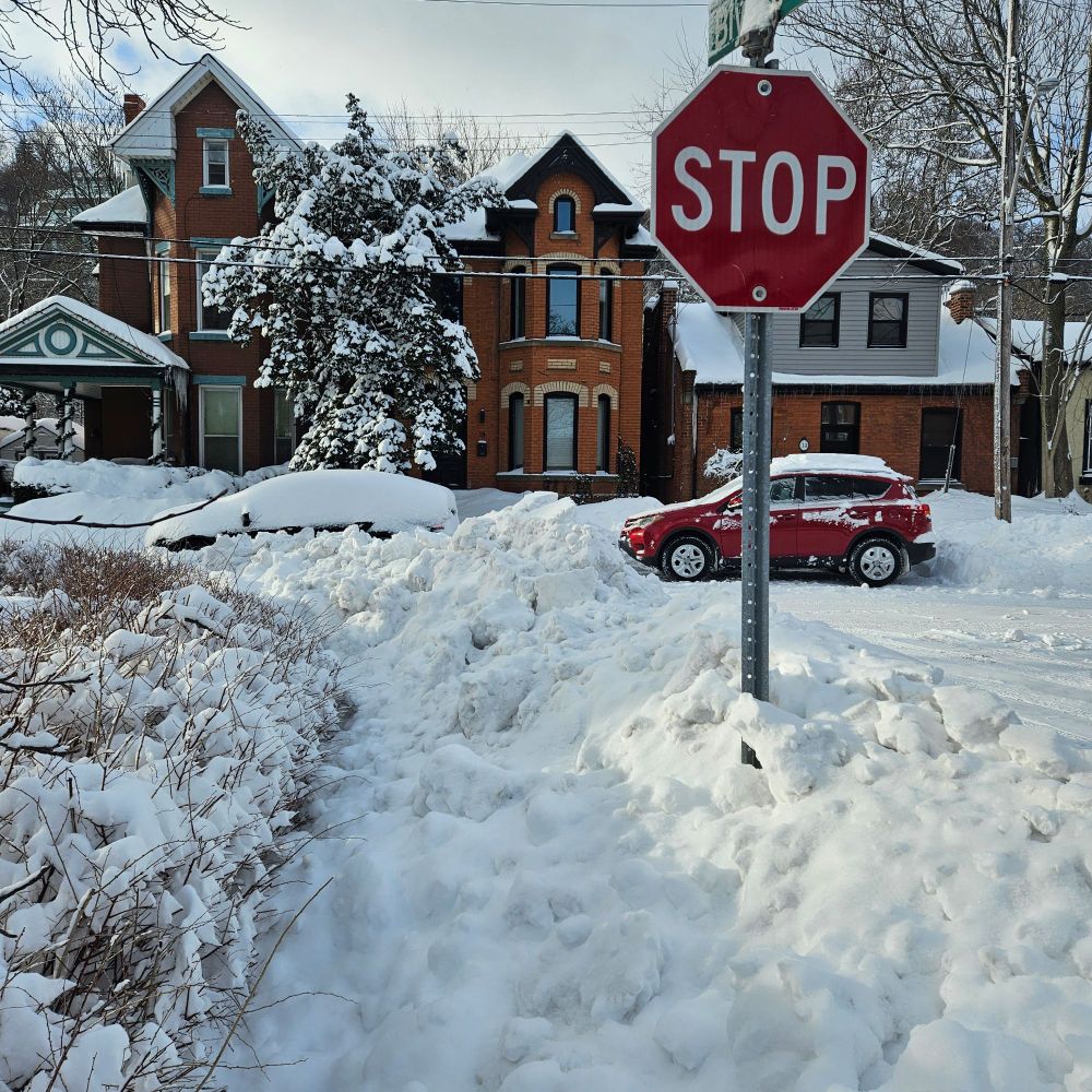 A bank of snow and ice, nearly six feet in height, on a residential street corner.