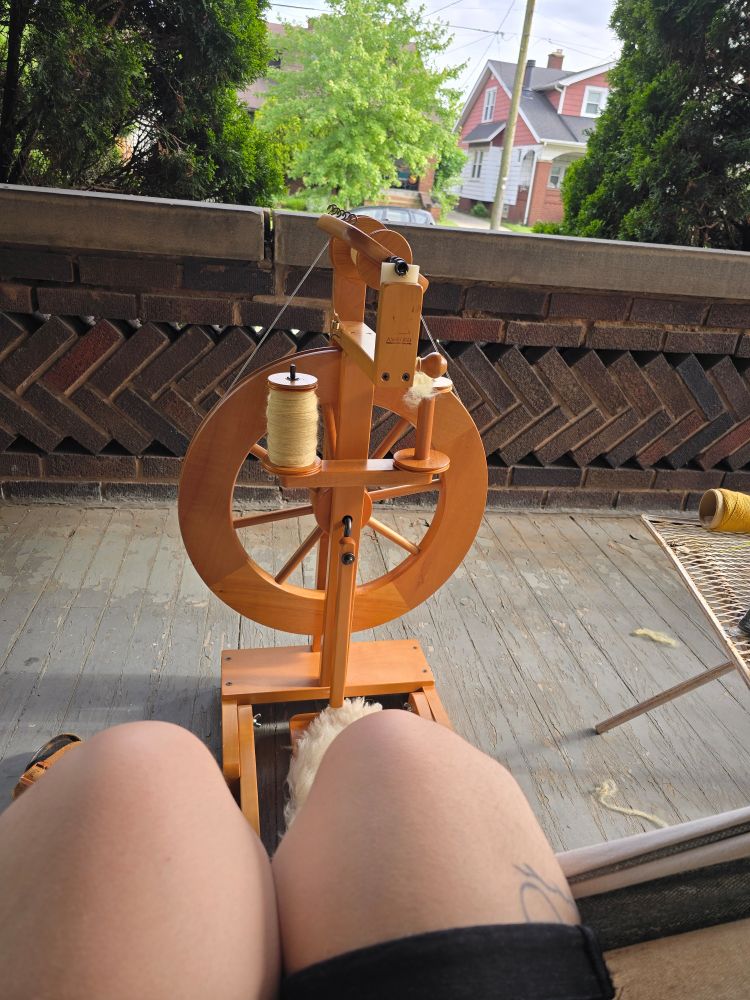 A spinning wheel on a porch with AV's knees just in frame sitting on a hammock