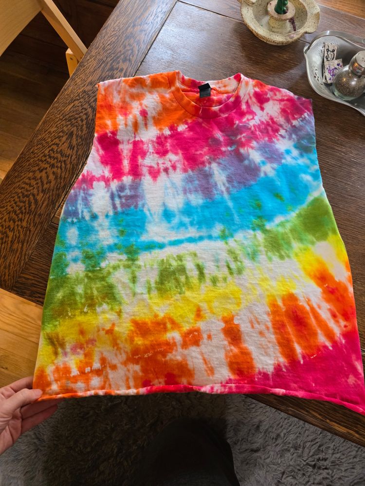 A tie dyed rainbow shirt with the sleeves and bottom cut off on a wooden table
