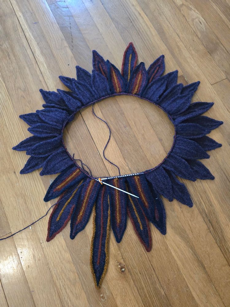 A knit work in progress. A bunch of dark feathers knit in the round on circular needles making up the Lapwing Collar.