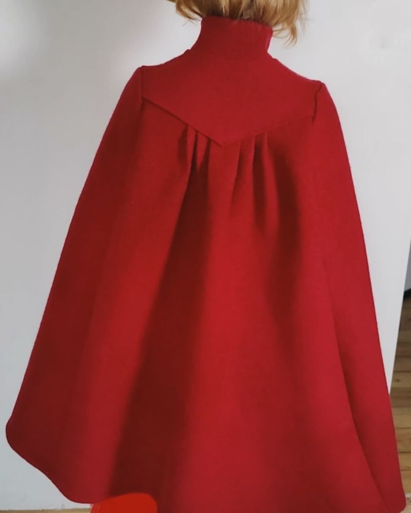 back view of red mid-length cloak showing the drape of five pleats at the centre back