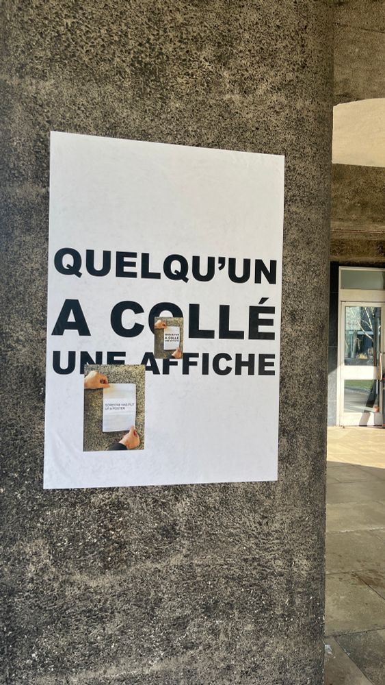 A large poster in French on a pillar of the RFB reads “Quelqu’un a collé une affiche”. Smaller superimposed posters in French repeat the same words, and an English poster translates the phrase: “Someone has put up a poster”.