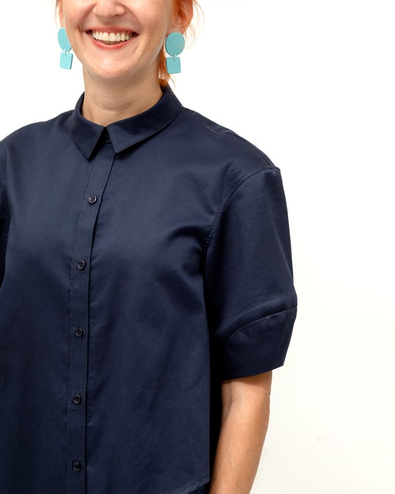 Close up of lantern sleeve on navy blue collared shirt worn on model standing against a white background 
