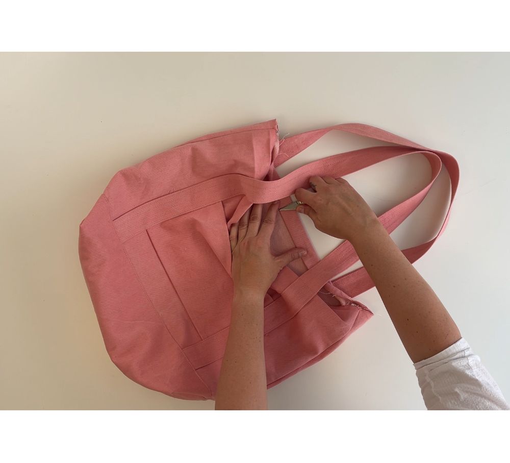 Pink canvas bag on white background with hands showing how the opening will be stitched 