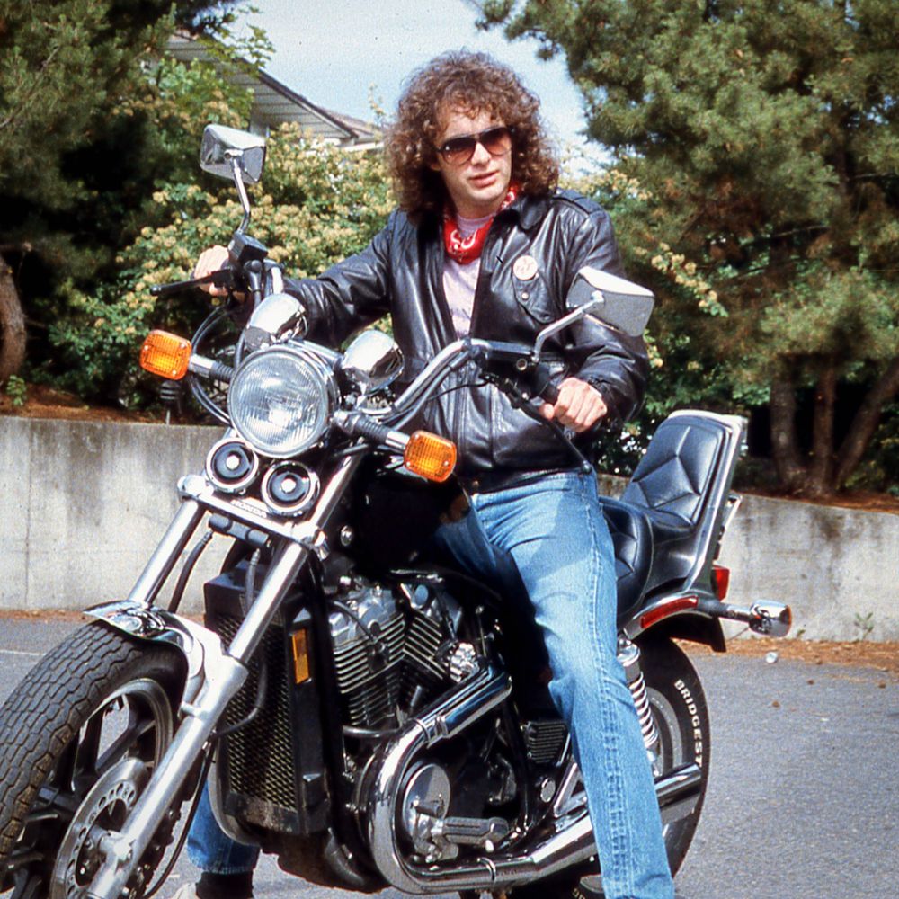 Man with long hair and black leather jacket on motorcycle 