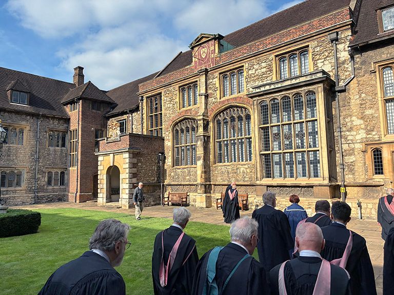 Fellows and members of the Burgon Society, in academic gowns and hoods, walk from a courtyard to the entrance of The Charterhouse for the afternoon session after Congregation on Saturday, 11 October, in London. 