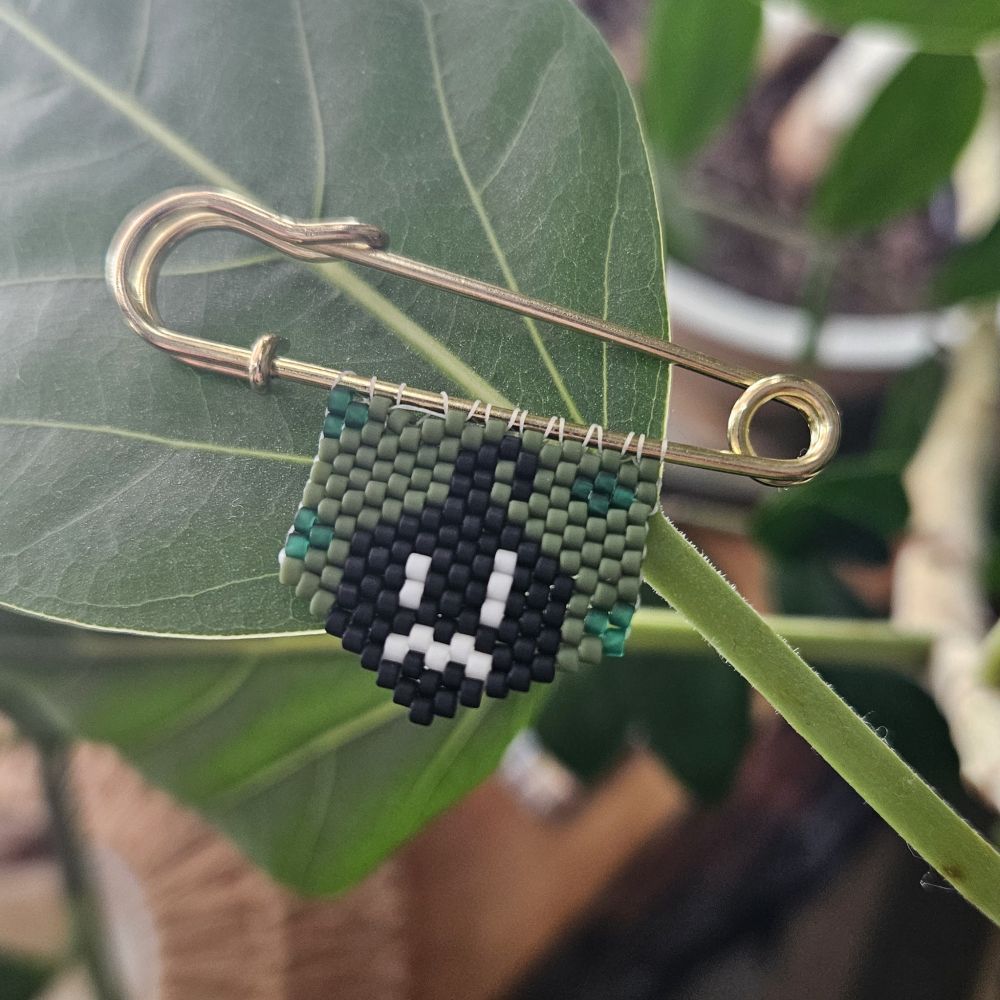 A beaded picture of krobus from video game stardew valley on gold pin.