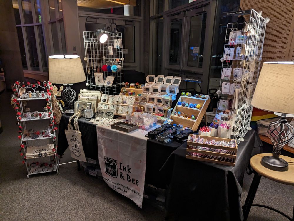 A table filled with ttrpg dice and accessories, bug jewelry, and other resin creations.