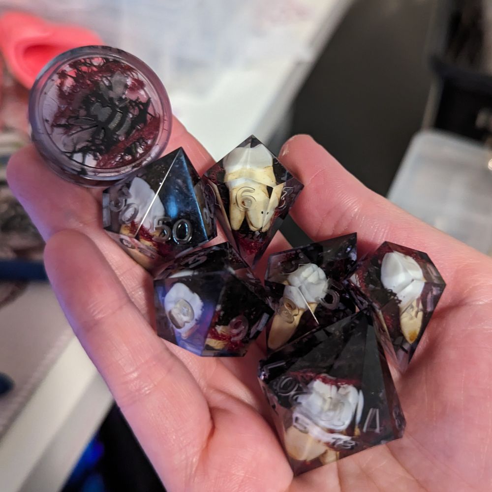 7 dice with black moss and red celosia with fake human teeth held in a hand.