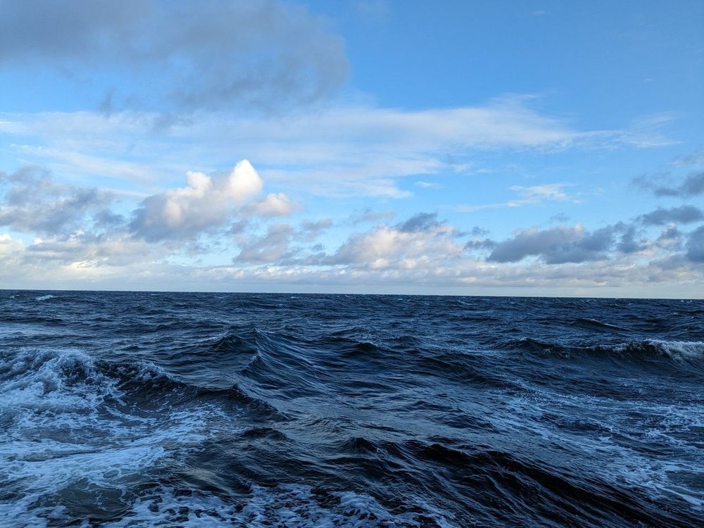 Von einem Schiff aus gemachtes Foto. Zu sehen sind Wellen und ein blauer Himmel mit Wolken.