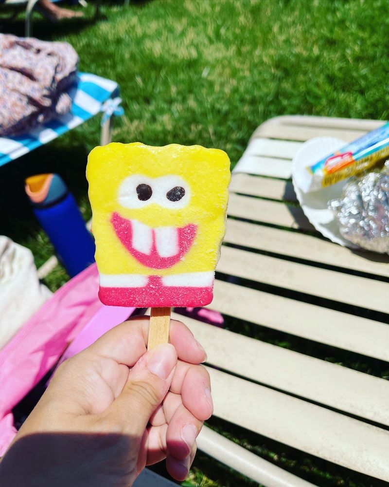 A hand holding a yellow popsicle shaped like a surprisingly identifiable Sponge Bob SquarePants 