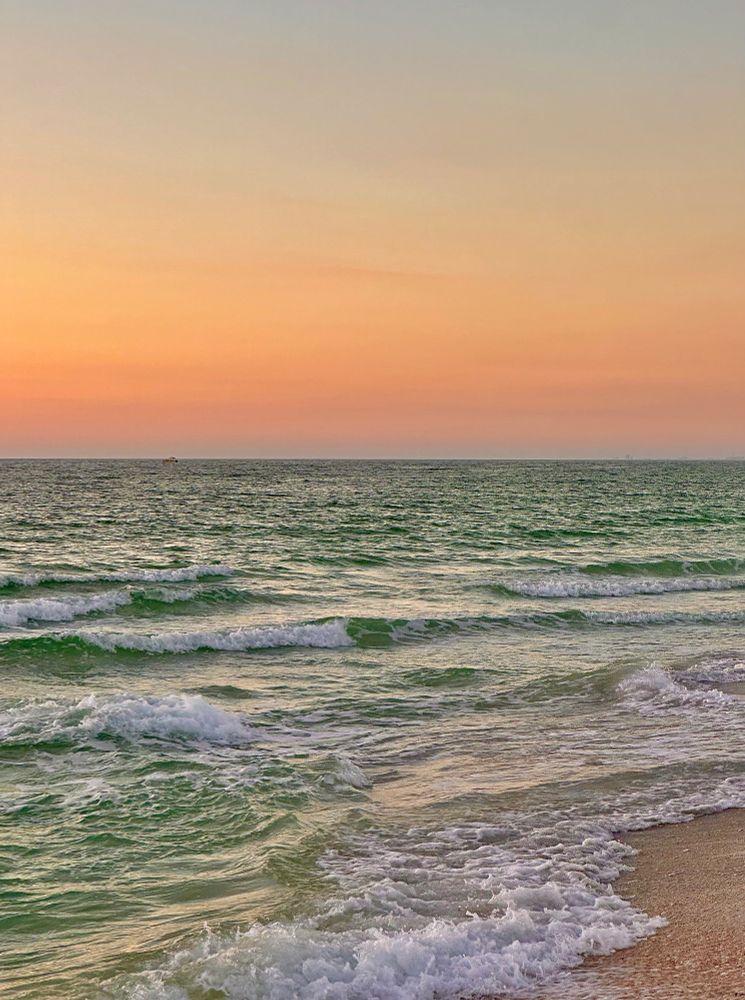Pastel orange color sunset afterglow over the horizon with gentle waves crashing into the beach 