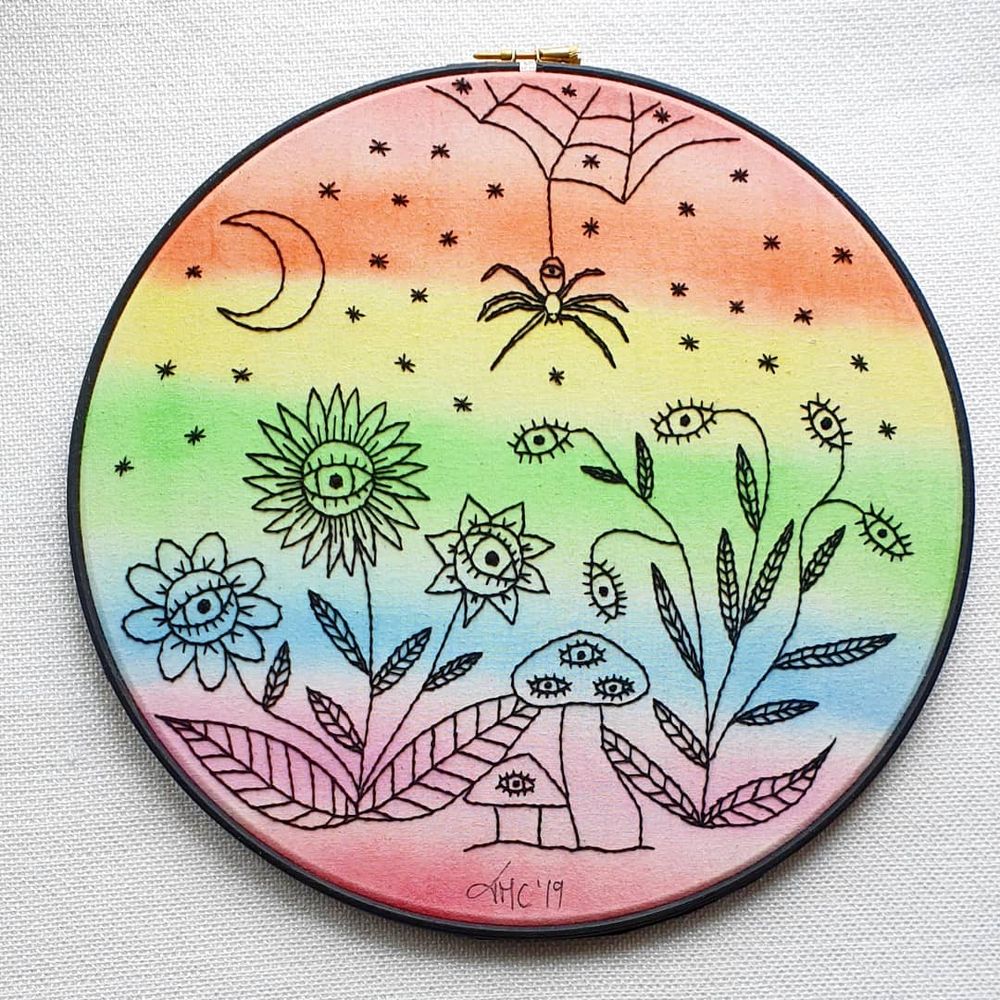 Eye Spy from the Feeling The Gaze (2019) collection by Tasha Darcy (with old signature)

A large black embroidery hoop frame that has been set with fabric that has been painted in rainbow colours, on the canvas has been stitched in black thread an assortment of flowers and fungi that all have eyes, at the top is a small spider's web from which a one eyed spider hangs, in the sky is a crescent moon and lots of little stars that look like tiny spiders.