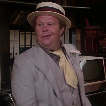 Ned Beatty as Otis in Superman (1978). He's wearing a grey suit, straw boater hat and a yellow tie with a knot the size of a grapefruit and a blade that is about 5 inches long, terribly short.