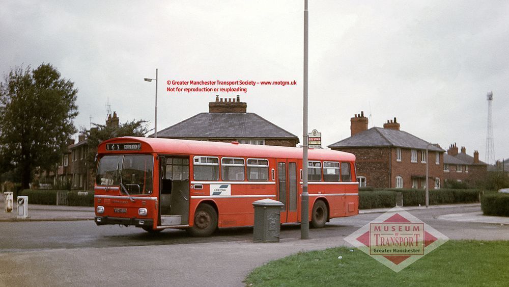 A red 1970s single decker bus waits at a bus stop in what appears to be a housing estate. The destination reads '123 Corporation Street' and the bus is parked next to a bus stop flag that's attached to a very tall street lamp. In the far background on the right, we can see what looks like a tall industrial flood light pylon.