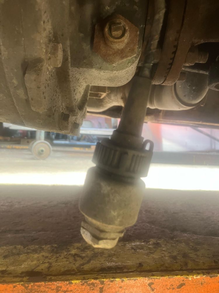 A view underneath a bus shows a speedometer drive, snapped off at one end, nagging down below the bus.