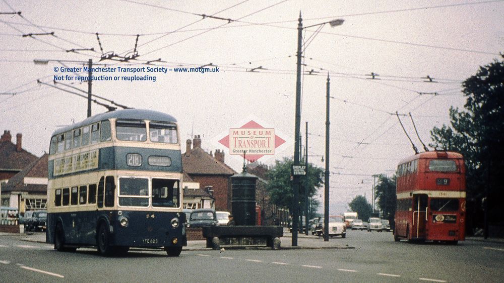A blue trolleybus, running under twin wires above the road, is on the left of the photo: while on the right we see a red trolleybus heading away from the camera.
