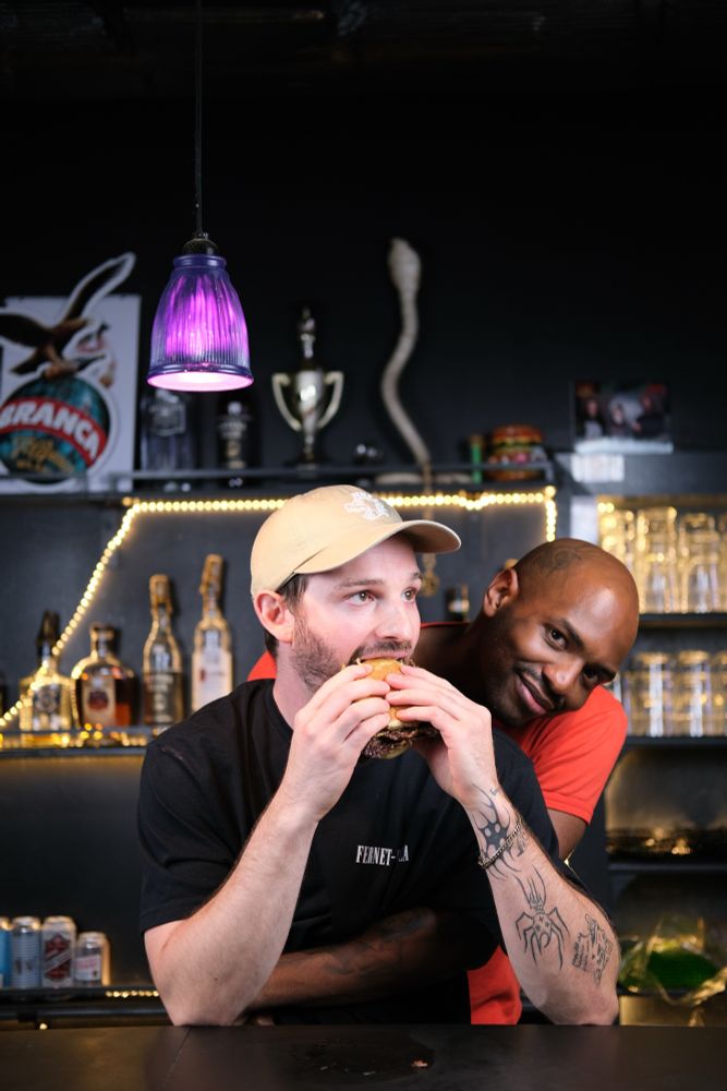 Two very handsome gentleman hugging while enjoying a burger