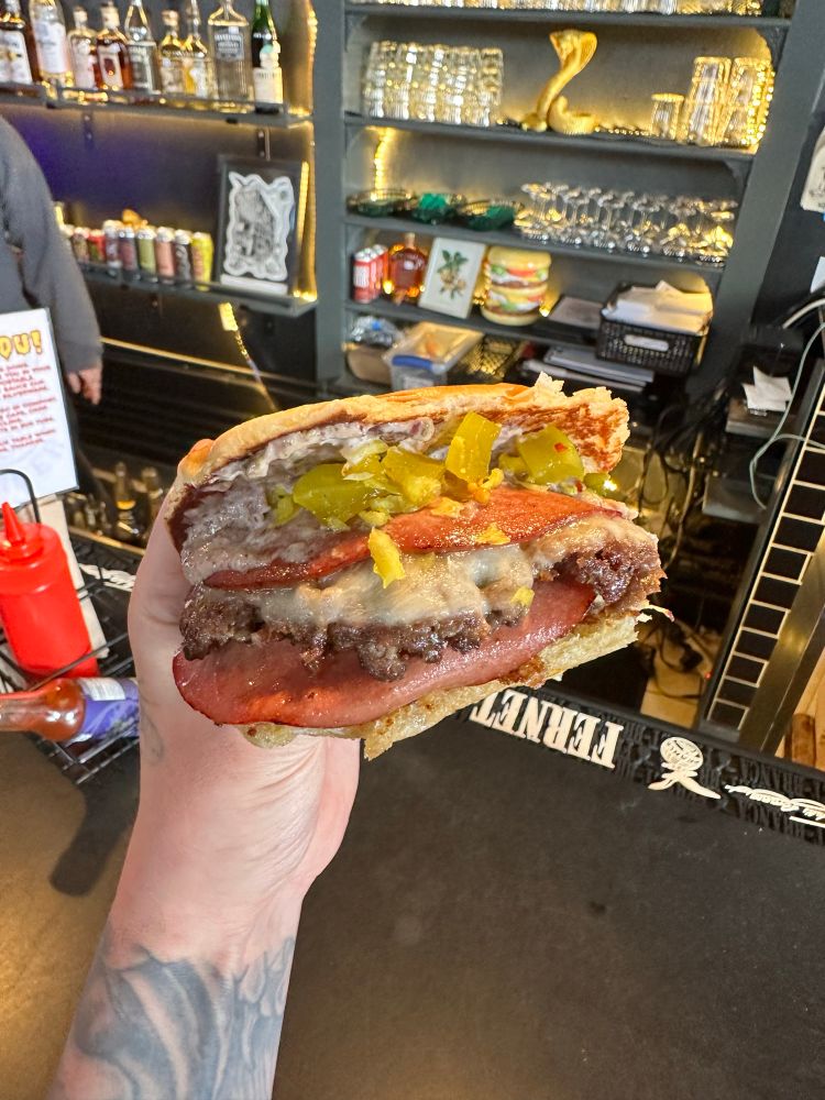 A hand holding the new RVA Muffuletta burger 