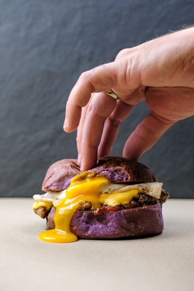 A hand popping the runny egg yolk on a Wake ‘n’ Snake breakfast sandwich