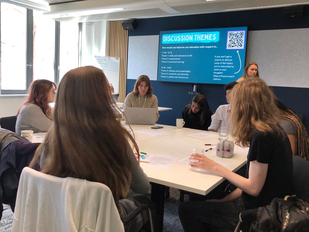 A group of young people sit around a table, discussing solutions to issues in their education
