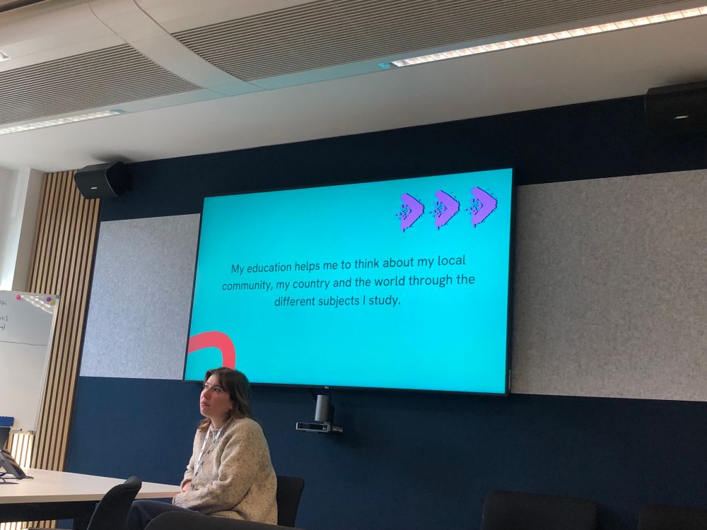 A young woman sits in front of a Smart board reading “My education helps me to think about my local community, my country and the world through the different subjects I study”
