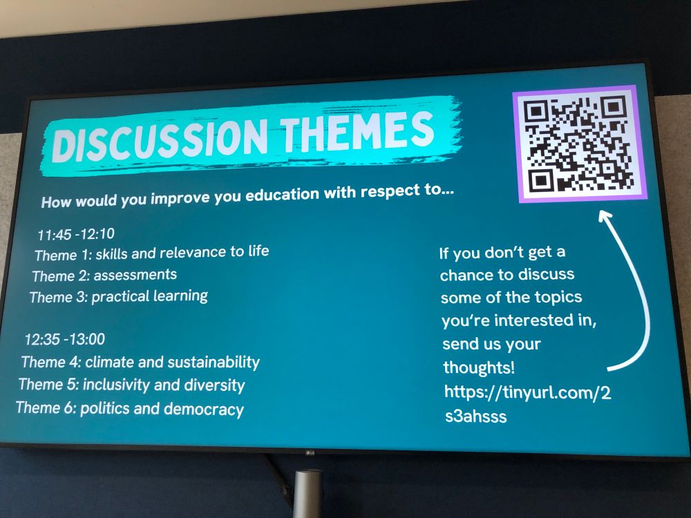 A Smart board reads
“Discussion themes
How would you improve your education with respect to…
Theme 1: skills and relevance to life
Theme 2: assessments
Theme 3: practical learning
Theme 4: climate and sustainability 
Theme 5: inclusivity & diversity
Theme 6: politics and democracy

If you don’t get chance to discuss some of the topics you’re interested in, send us your thoughts! https://tinyurl.com/2s3ahsss “