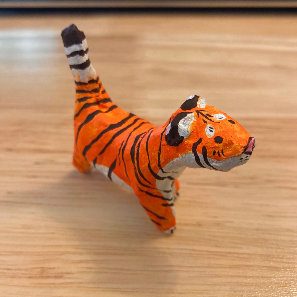 A small, lumpy tiger made out of papier-mâché and painted with acrylic gouache.