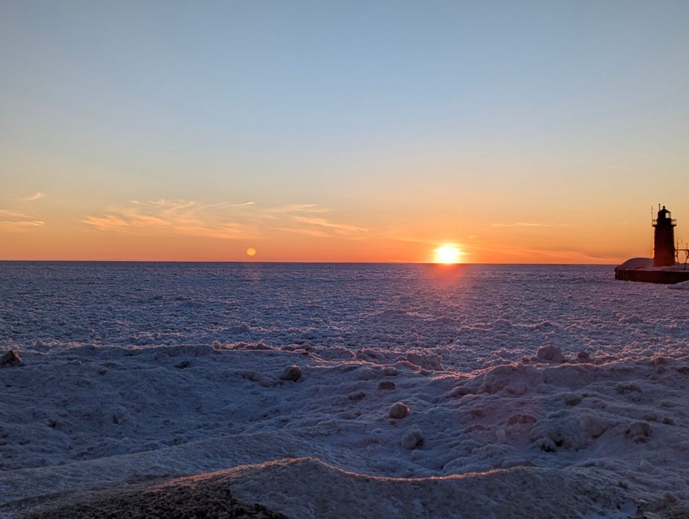the sun setting over the frozen Lake Michigan with a little lighthouse in the foreground on the right