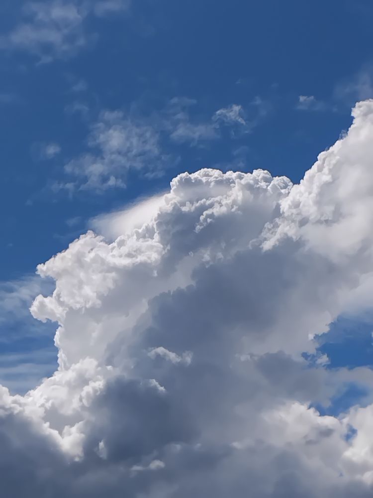 A towering cumulus cloud against the blue skies, near its peak whisps of a cap cloud are still visible signalling a strong updraft.