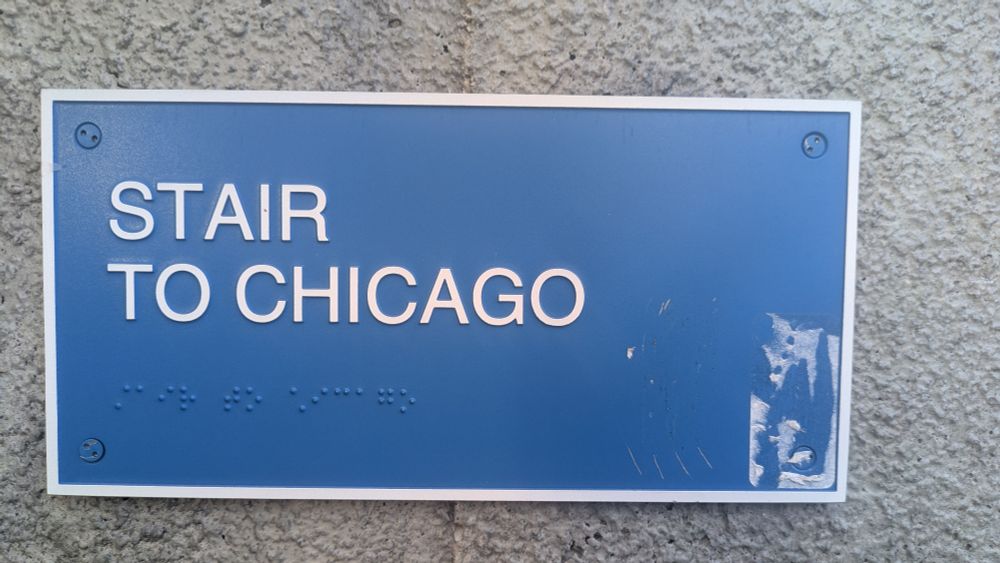 Blue sign with white border, white all caps text, and braille that says "STAIR TO CHICAGO"