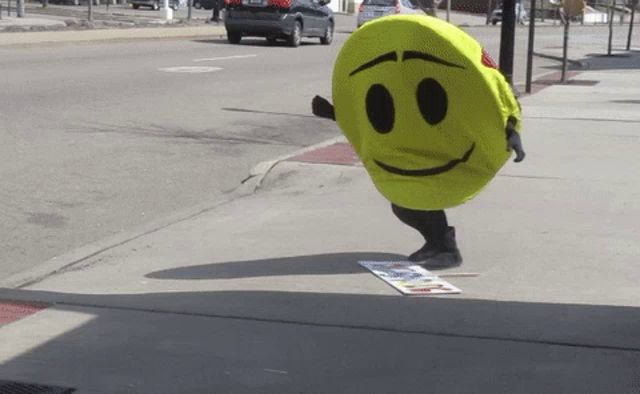 a person dressed as a yellow smiley face is walking down the sidewalk