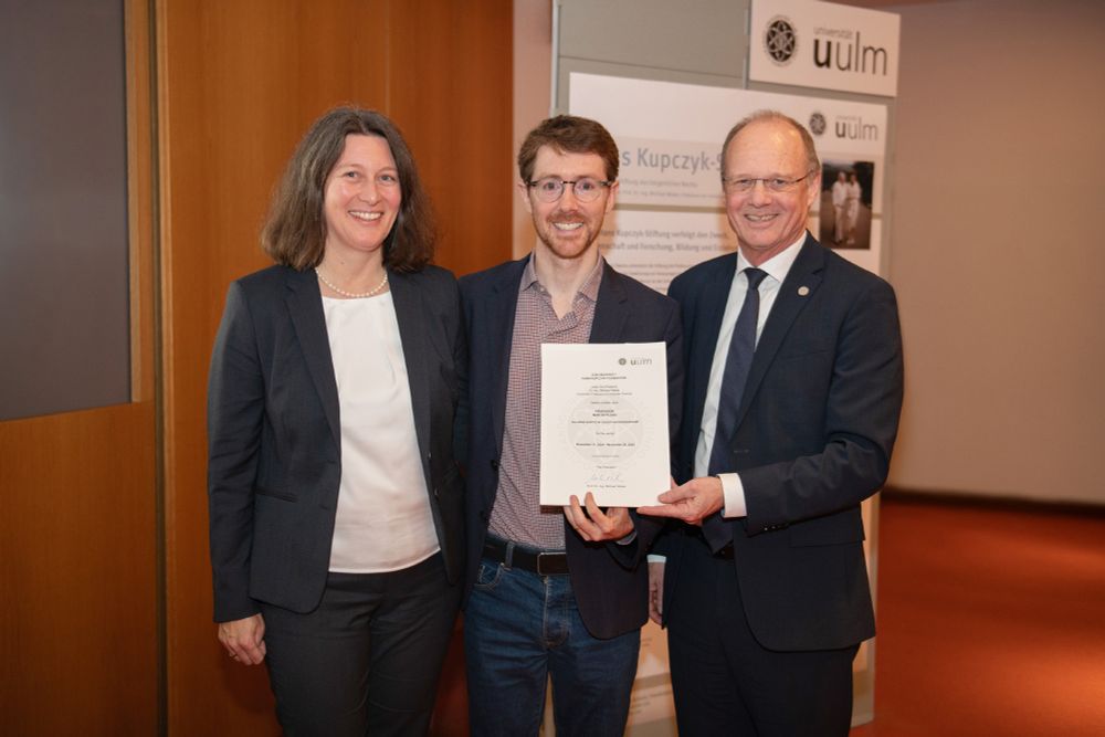 Prof. Martin Picard (Mitte) mit Prof. Iris-Tatjana Kolassa und Uni-Präsident Prof. Michael Weber im Senatssaal der Uni Ulm. Sie zeigen die Ernennungsurkunde zum Gastprofessor. 