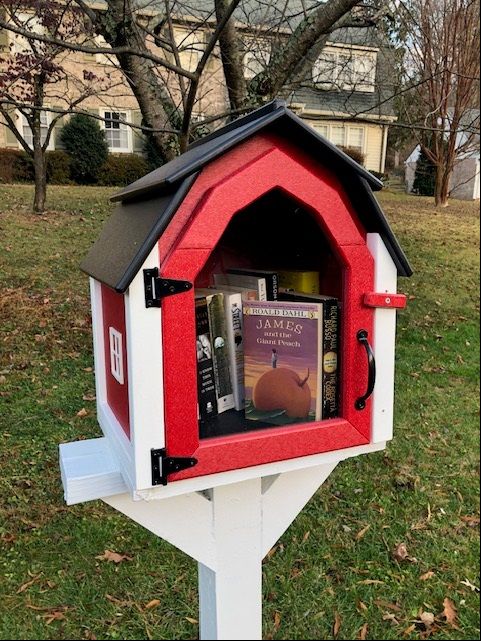 Little library in the shape of a red barn with white trim and a black roof.  Books inside the library including the book, James and the Giant Peach.