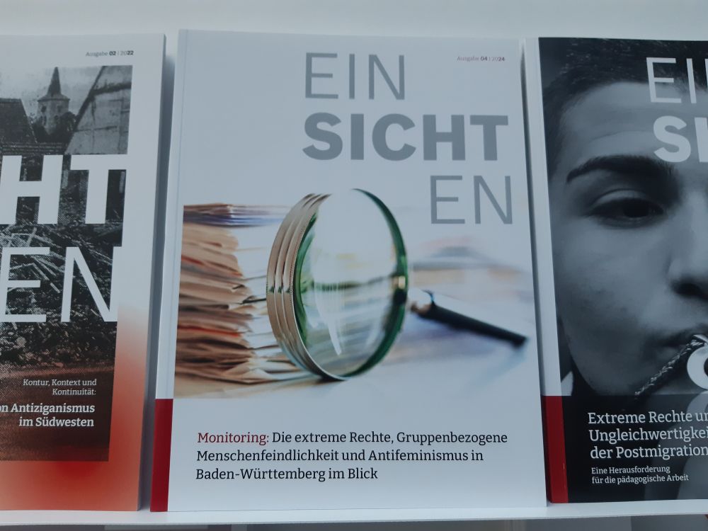 Das Foto zeigt das Cover der vierten Ausgabe des Magazins Ein Sicht en. Das Magazin wird von der Fachstelle mobirex herausgegeben. Zu sehen ist darauf eine große Lupe vor einem Stapel Akten. Das Thema der Ausgabe lautet: "Monitoring: Die extreme Rechte, Gruppenbezogene Menschenfeindlichkeit und Antifeminismus in Baden-Württemberg im Blick." Farblich ist das Cover überwiegend weiß gestaltet mit ein paar kleinen roten Elementen. Links und rechts dieses Covers sieht man die Cover der 2. Ausgabe (zum Thema Antiziganismus) und der 3. Ausgabe (zum Thema extreme Rechte in der Postmigrationsgesellschaft). mobirex ist Teil des Demokratiezentrums Baden-Württemberg und befindet sich in Trägerschaft der Landesarbeitsgemeinschaft Offene Kinder- und Jugendbildung Baden-Württemberg e.V. (LAGO).