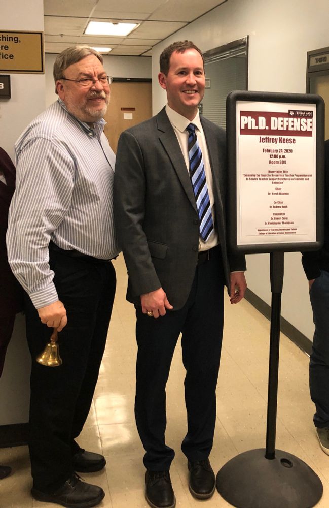 Dr. Waxman in a gray striped shirt and black pants next to me at my dissertation defense. He’s holding the bell we ring after a successful defense. 