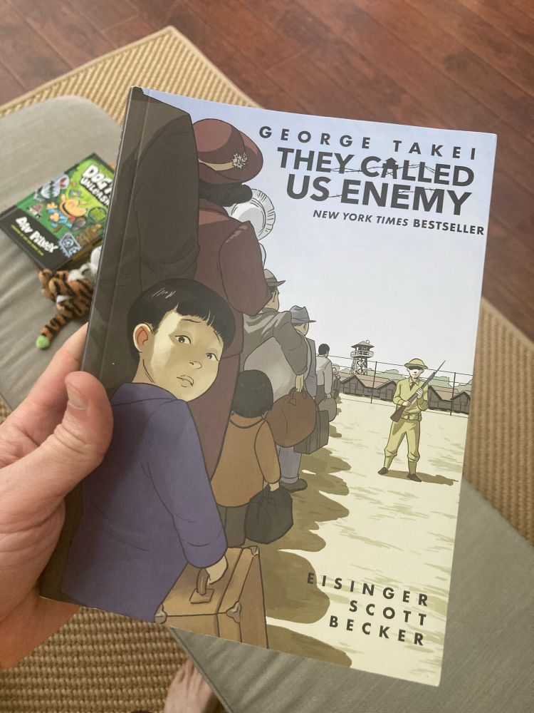 Cover of George Takei’s They Called Us Enemy” showing a young Japanese American boy in a line of people being sent to an internment camp guarded by a uniformed American soldier
