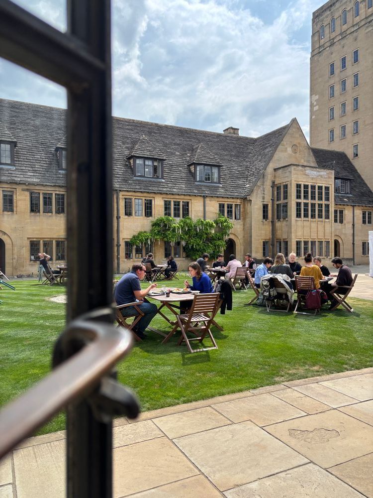 College members enjoy the outdoor seating in the Upper Quad of Nuffield College, with the tower and blue skies in the background.