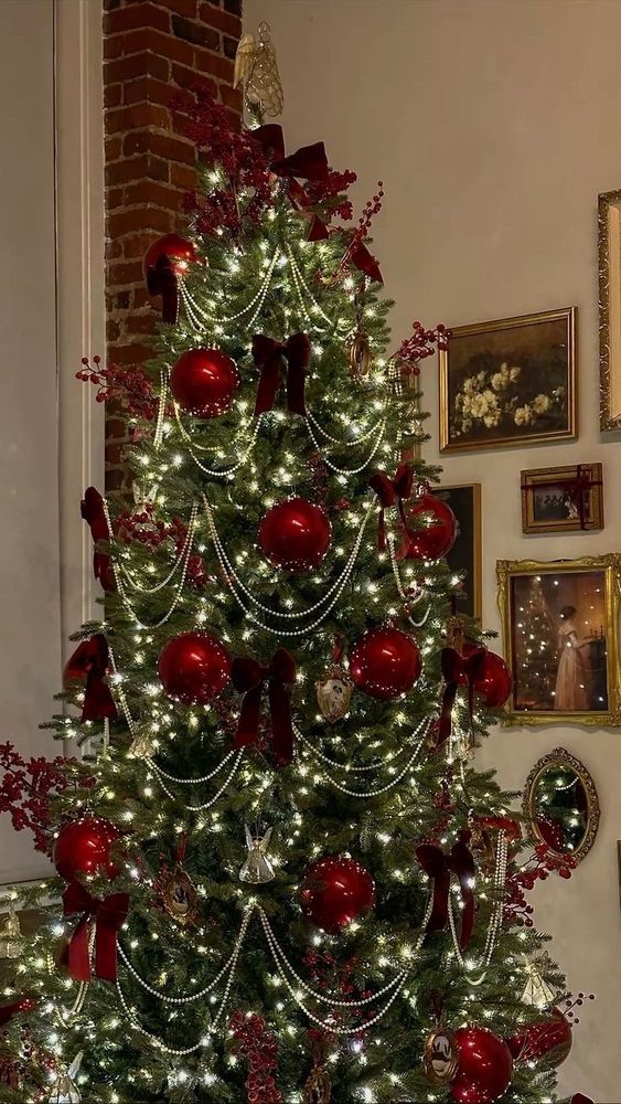 an elegant green christmas tree decorated with red ornaments, pearls, red ribbons, and angels