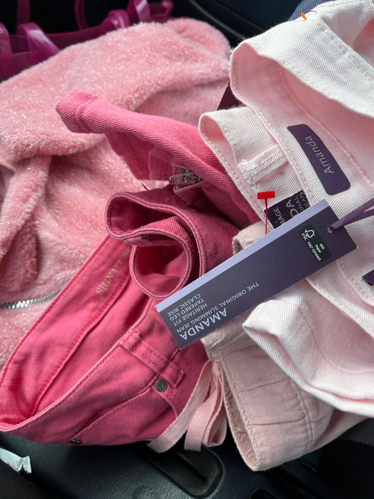 A photo of a pile of pink clothing from a thrift store that salem just acquired. One thing is a pair of jeans with a tag still on them 