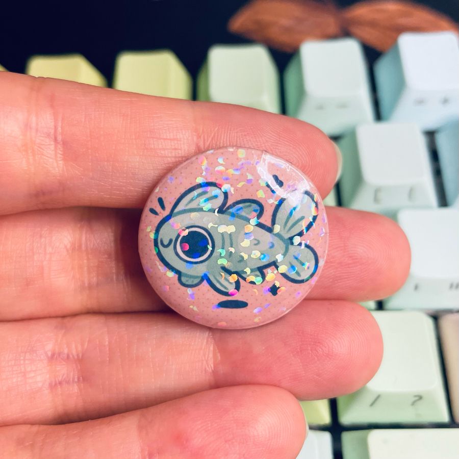 small fish pin being held against the backdrop of a keyboard