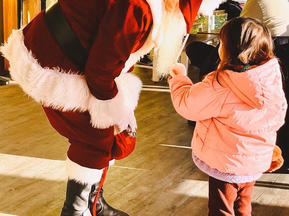 Santa Claus and a kid face each other where the kid holds the pompom ball of Santa’s hat. 