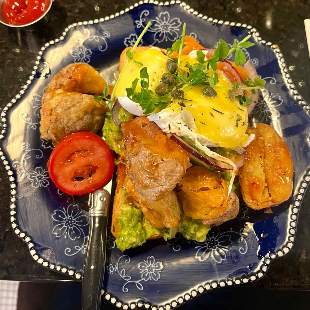 Brunch consisting of potatoes, guacamole, and salmon eggs Benedict with capers, red onions, and tomatoes. 