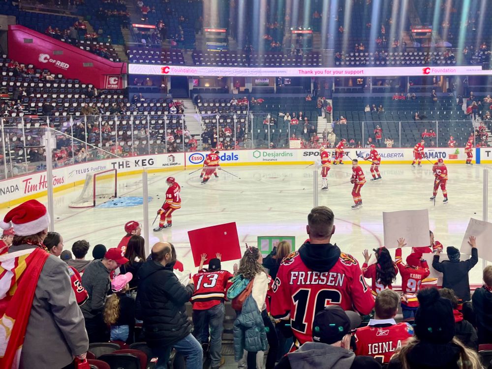 Calgary Flames warmups. Fans have their backs turned to the camera and are watching the hockey players on the ice.