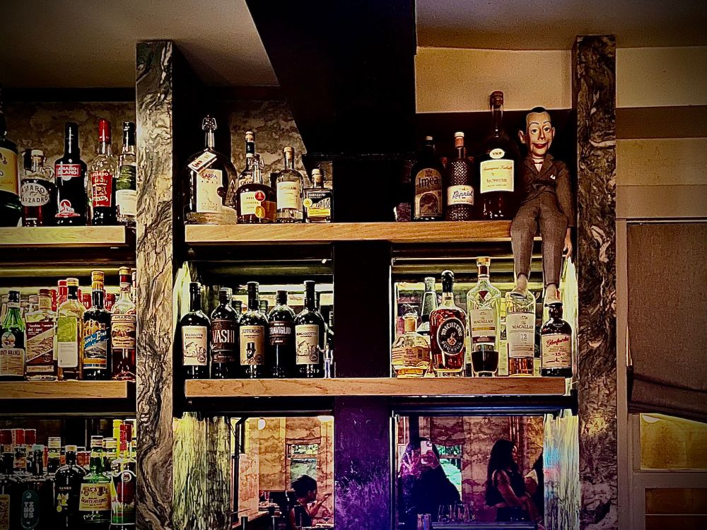 Various liquors on a bar with a ventriloquist dummy sitting at the end of the row. 